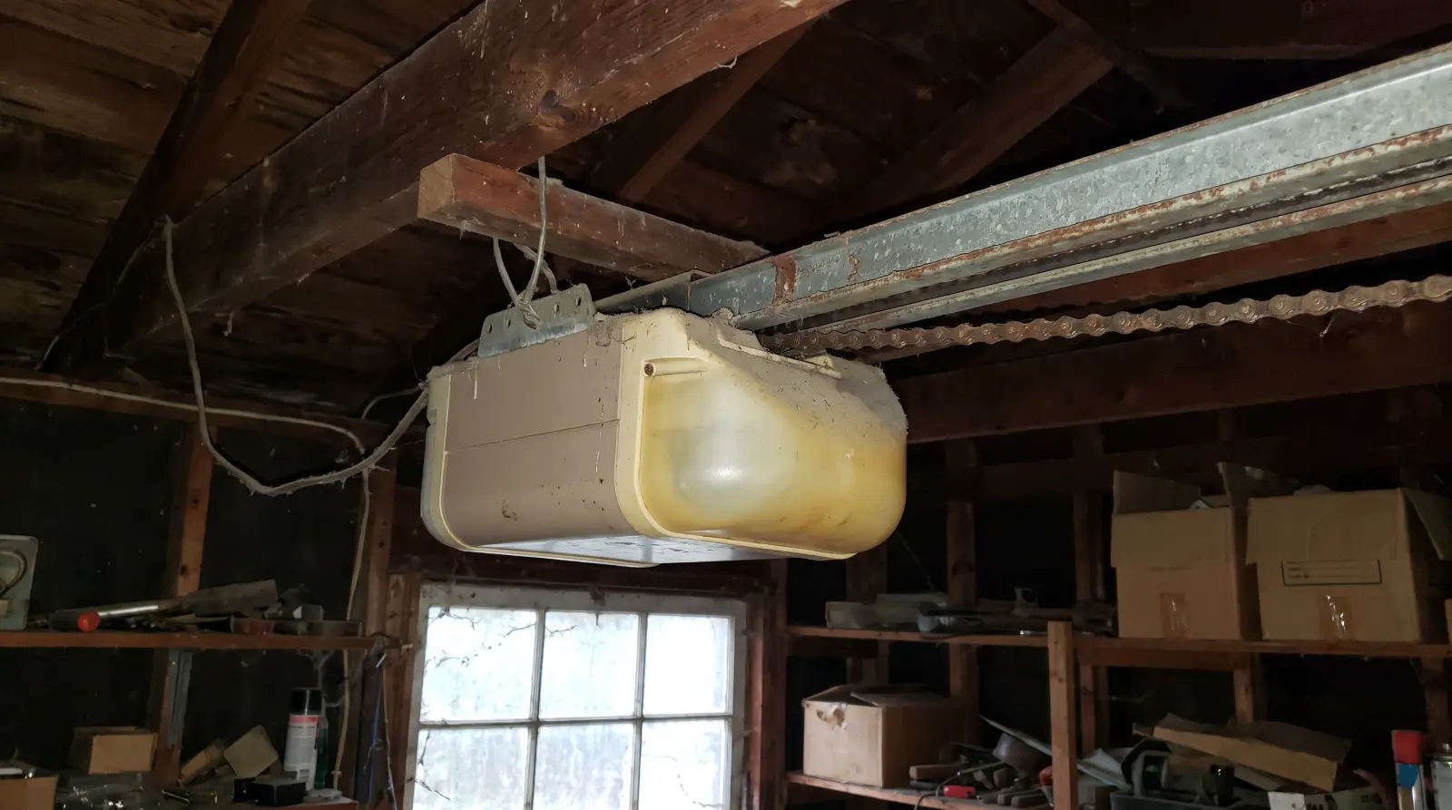 Older chain-drive garage door opener hanging from wooden ceiling joists